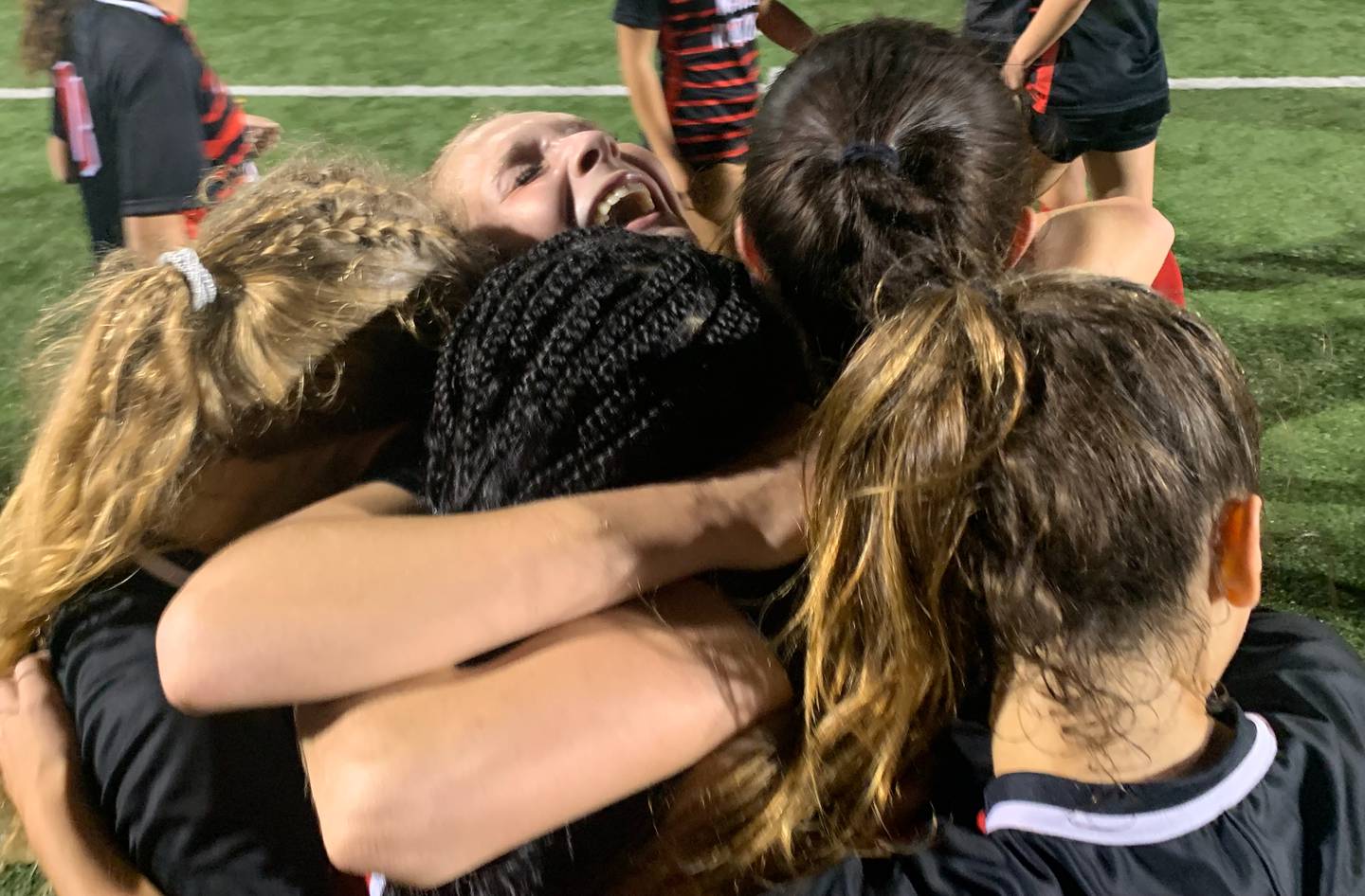 Sydney Feiler is hugged by her Mercy teammates after Saturday night's IAAM A Conference soccer championship game. The senior's goal with 11 minutes, 39 seconds left in regulation lifted the No. 2 Magic to a 1-0 victory over fourth-ranked McDonogh at Calvert Hall.