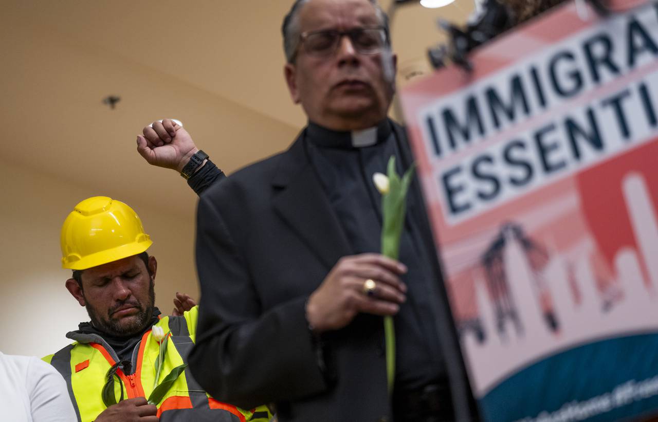 Pavel Mena, background, holds up a fist to show support while his colleagues speak. Construction workers honored the Key Bridge victims during a press conference on March 28, 2024 at CASA's Baltimore worker center. They held white flowers and raised their hands in solidarity.