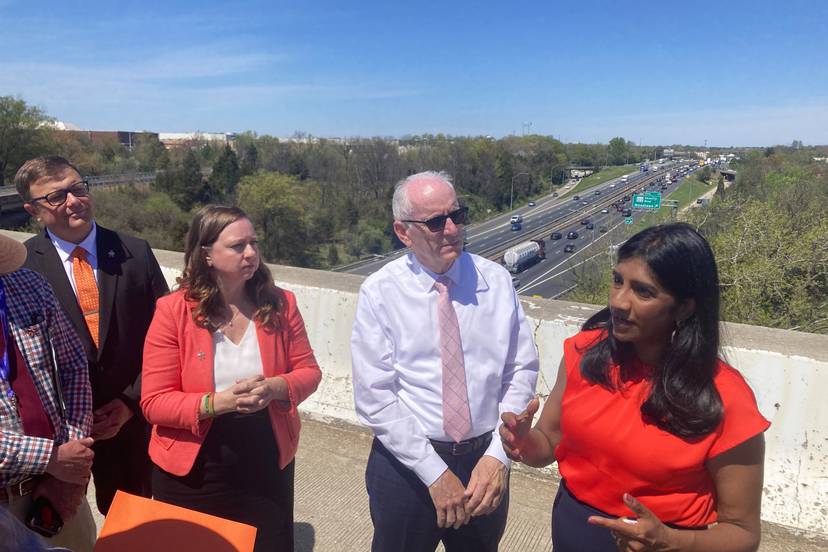 Four people stand and talk on a highway overpass with a large highway in the background.