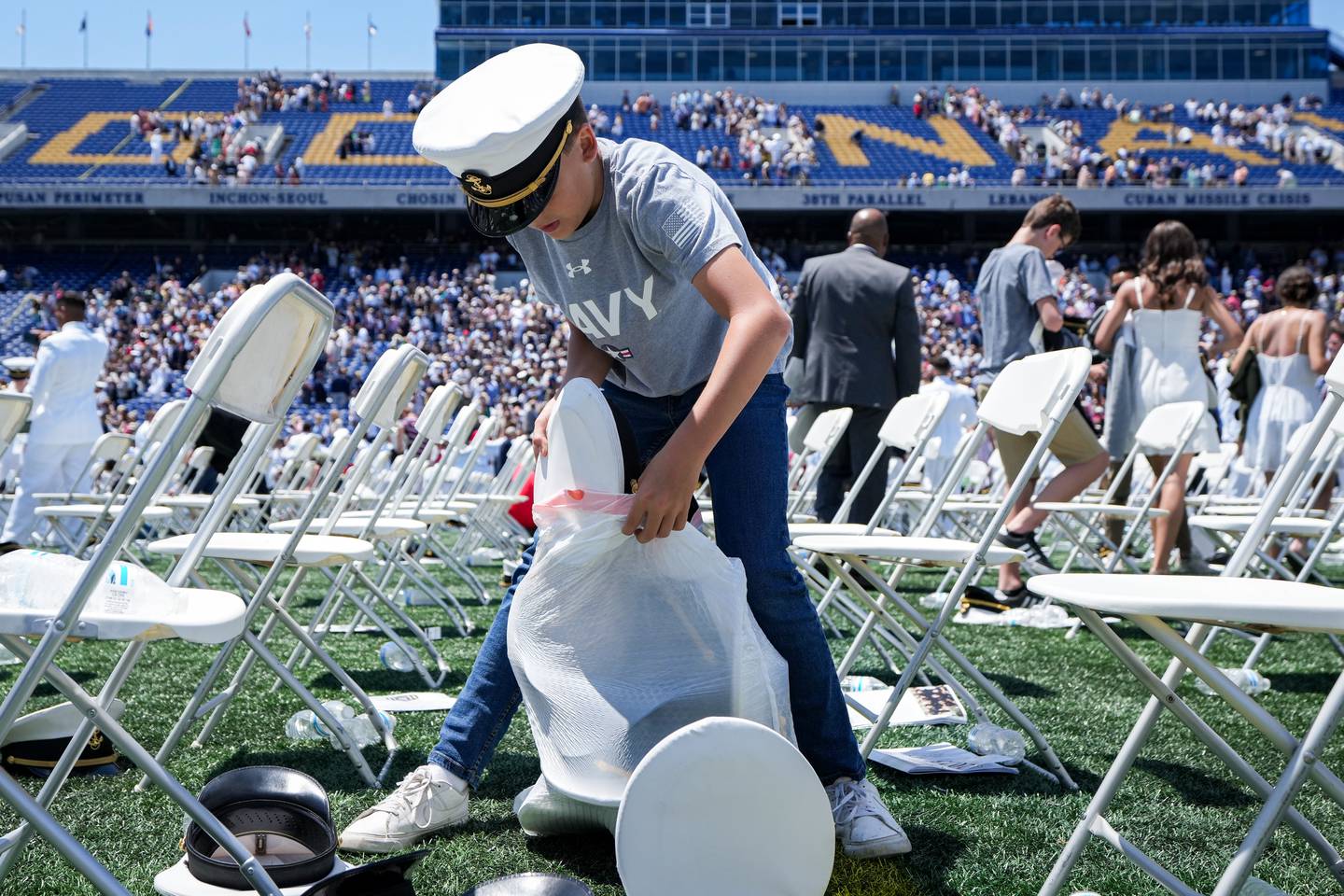 A young child collects discarded covers in a garbage bag at the conclusion of the U.S. Naval Academy’s graduation ceremony at the Navy-Marine Corps Memorial Stadium on May 26, 2023. The graduating midshipmen are commissioned as either an ensign in the U.S. Navy or a 2nd Lieutenant in the U.S. Marine Corps.
