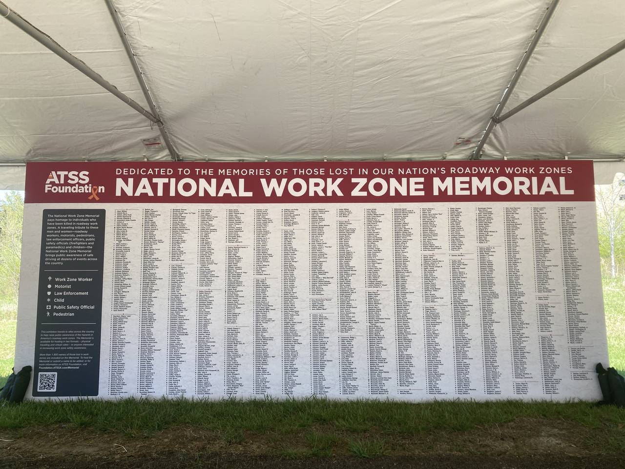 A large white sign displaying hundreds of names is displayed under a white tent.