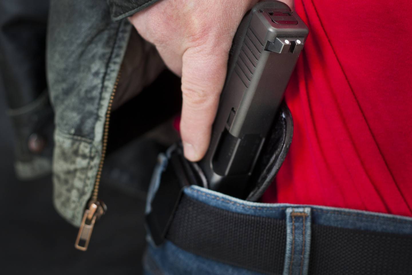 A caucasian man drawing his modern polymer (Glock) .45 caliber pistol from an IWB (inside the waistband) holster under his leather jacket.