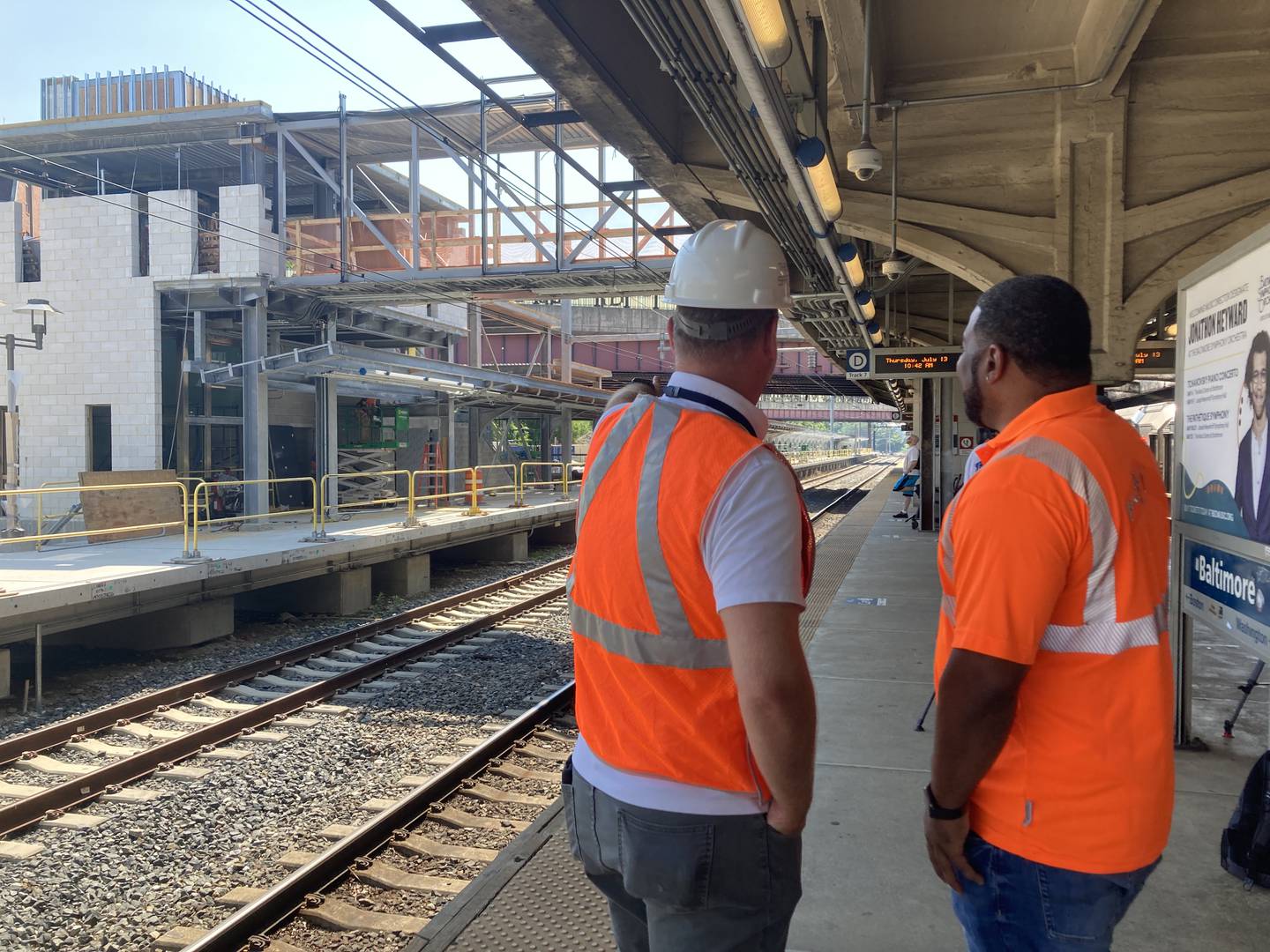 Two project managers with orange vests look on at construction for a train platform inside a station.