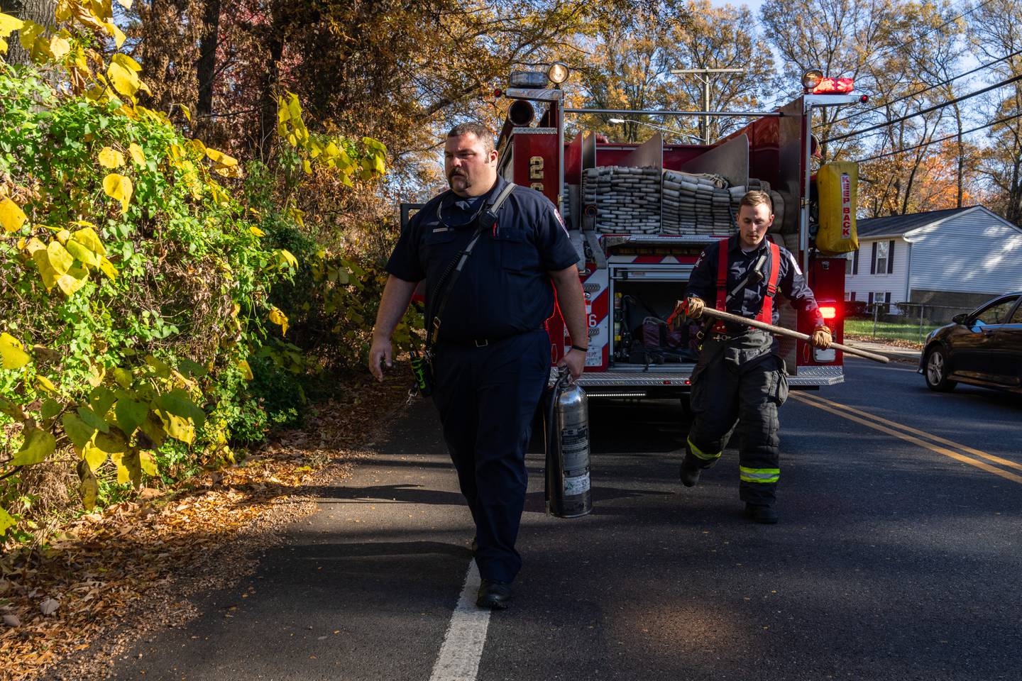 Prince George’s County firefighters Matt Fisher, left, and Jacob Smith bring out equipment to extinguish a smoldering piece of wood in the woods in District Heights, Md. on Tuesday, Nov. 14, 2023.