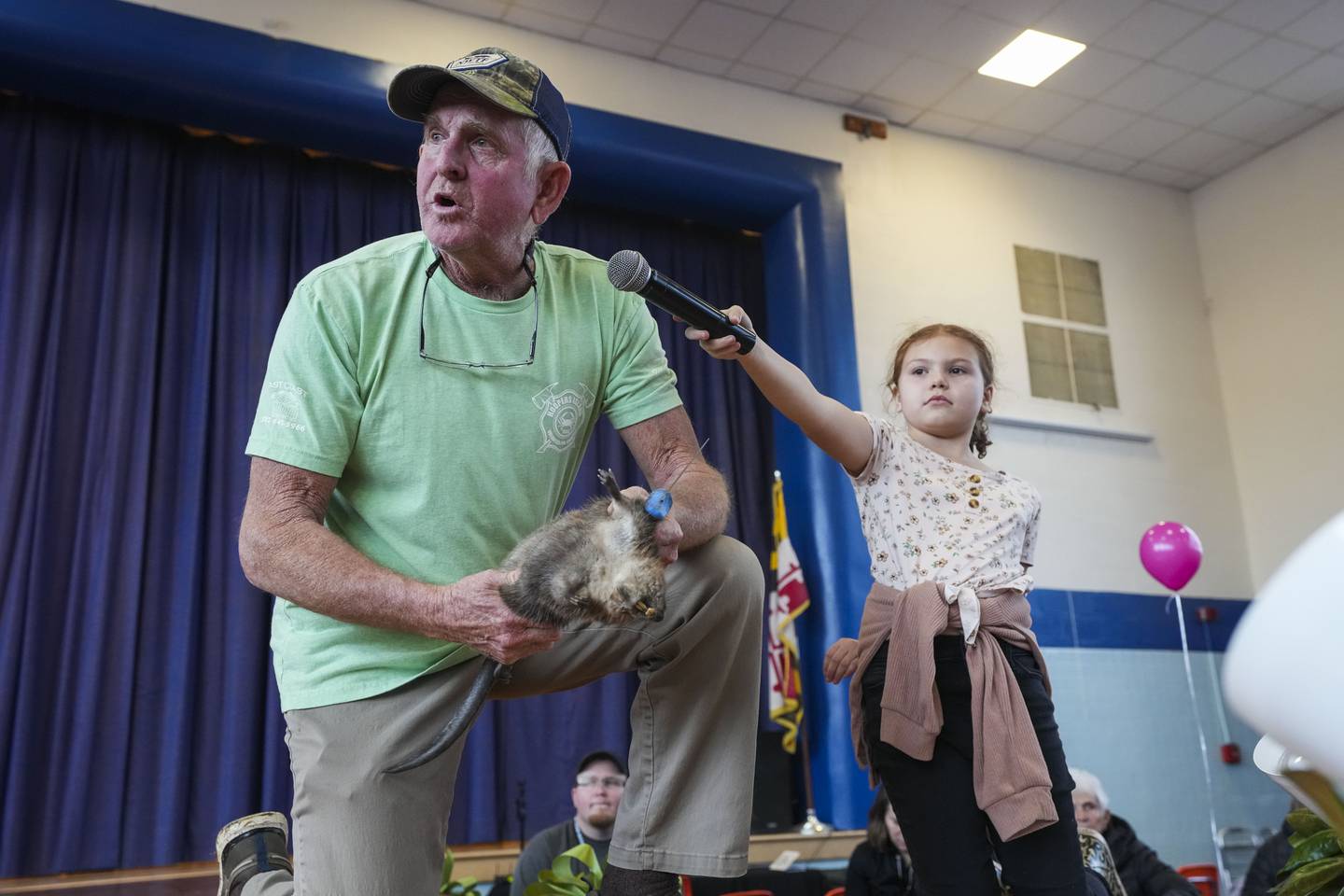 Kinsley Aaron, 10, holds the microphone for Buddy Flowers, 66, as he skins a muskrat for an audience explaining the process as he goes.