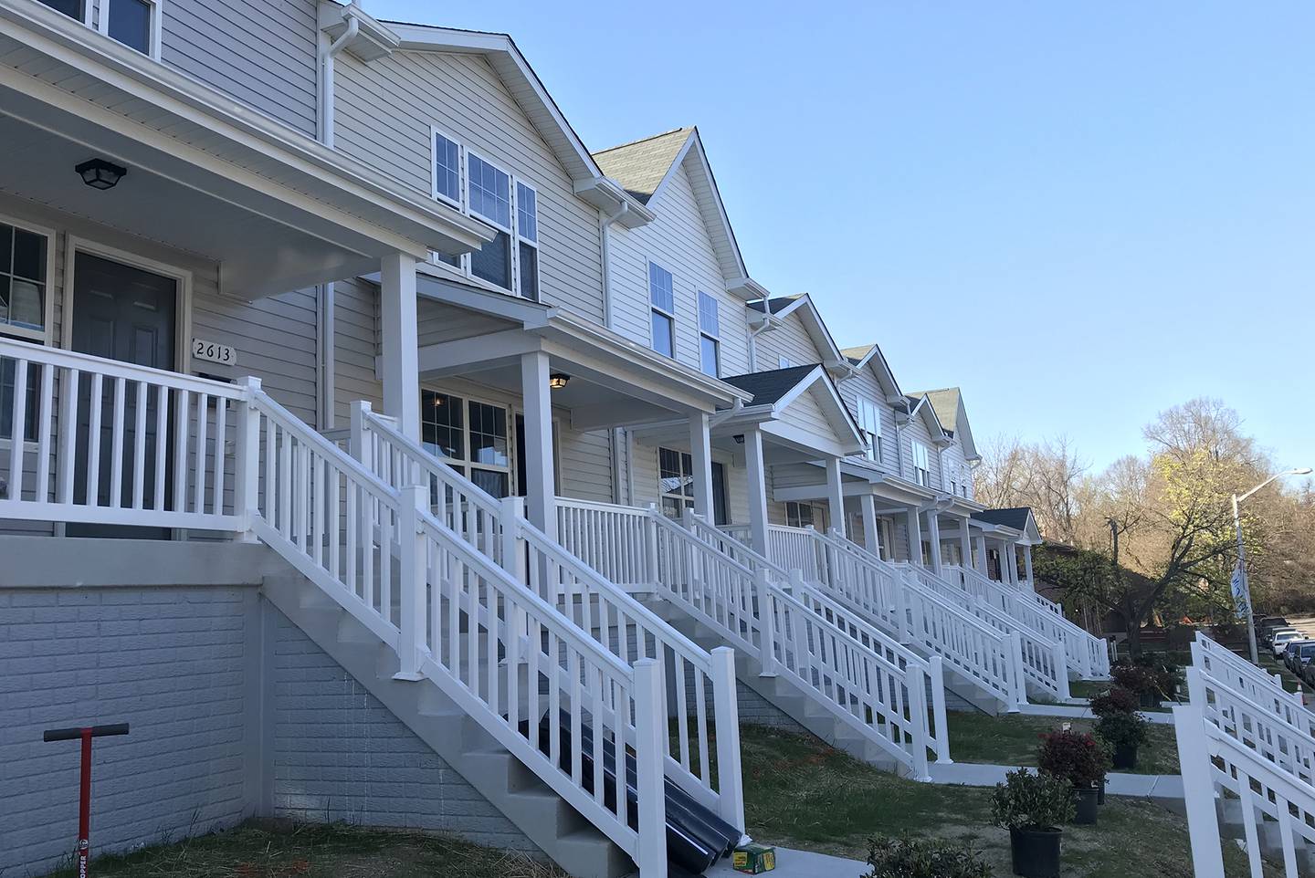Town homes painted in light colors with a clear blue sky and porches with white railings leading to neat front yards.