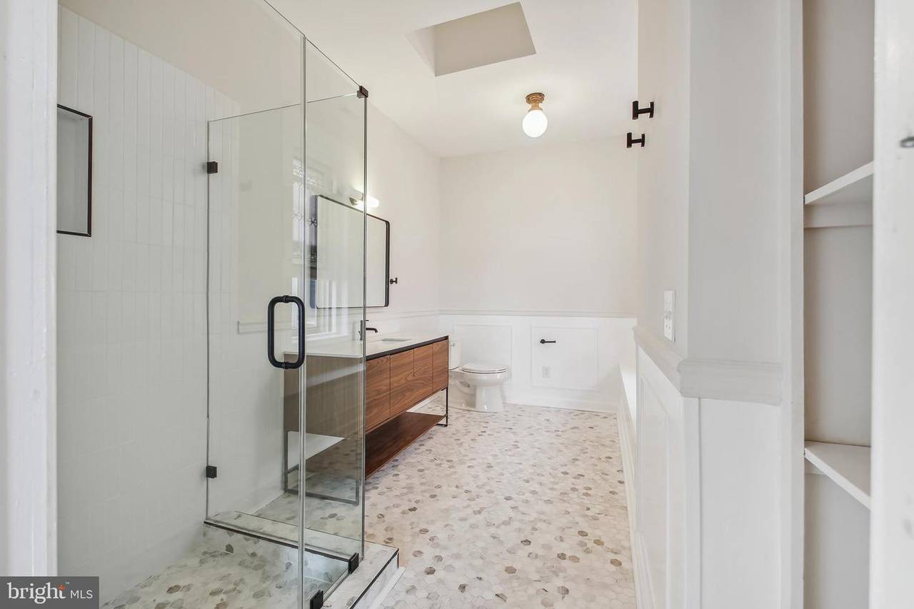 A photo of a large bathroom with a glass-walled shower, light gray walls, white wainscoting includes modern sink fixtures and a modern light fixture.