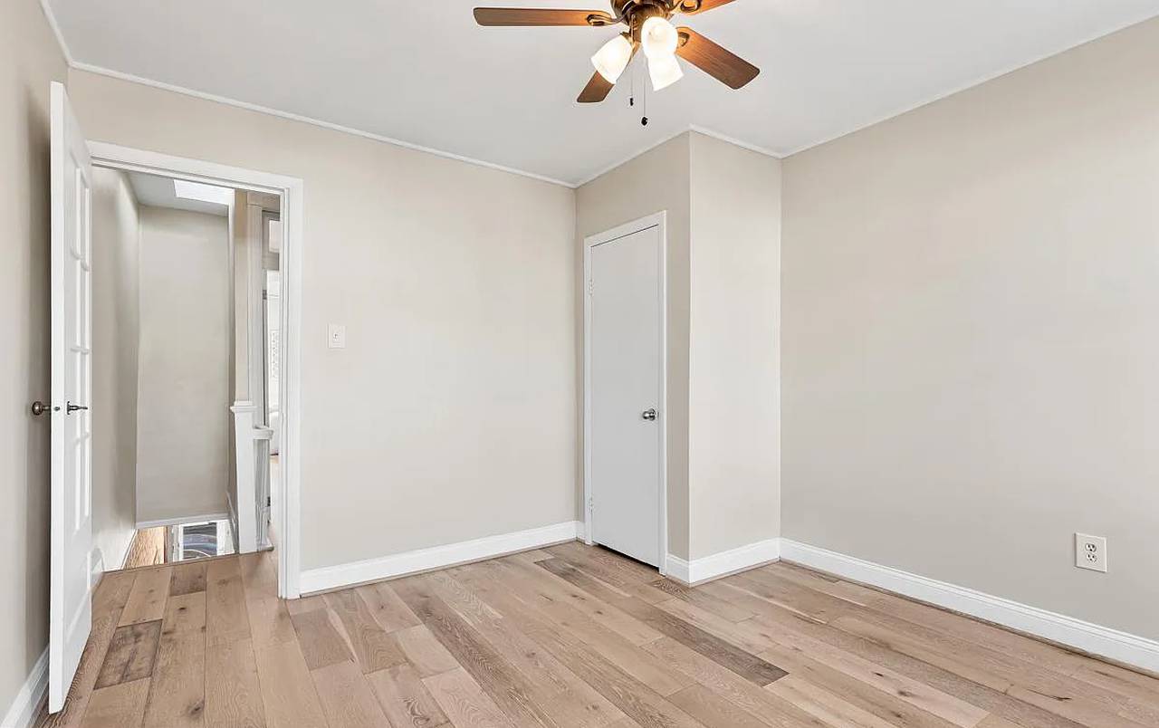 An upstairs bedroom with no furniture. There's hardwood floors with a light stain, beige walls and white trim.