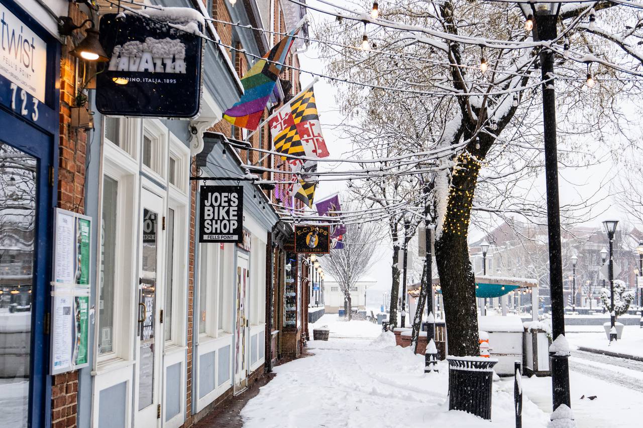 Snow falls on businesses with colorful flags outside their doors along S Broadway in Fells Point on Friday, Jan. 19, 2024.