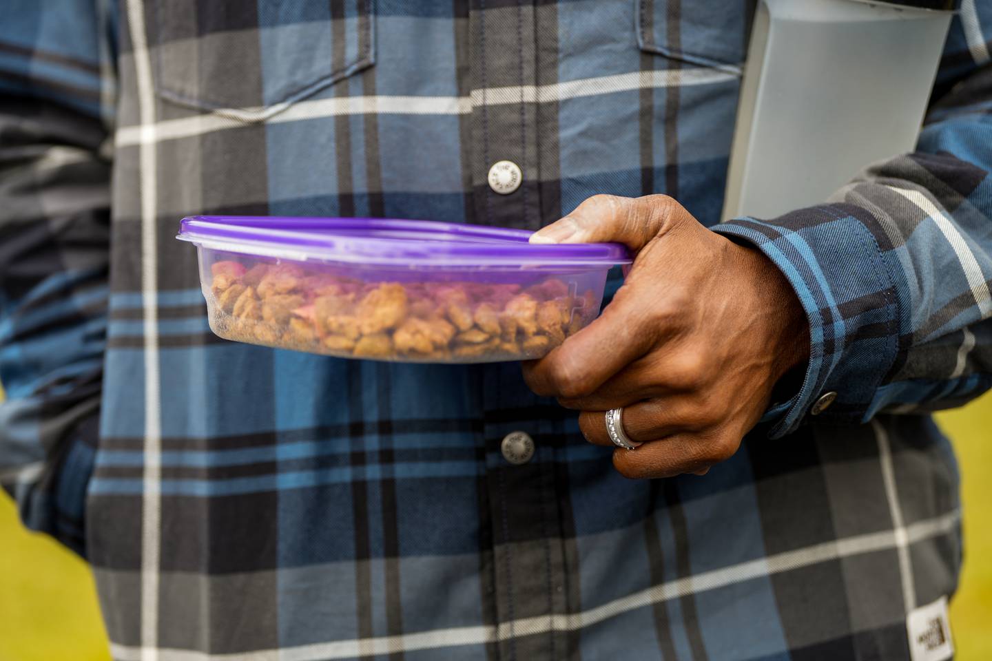 Man holds dog food in a plastic Tupperware container to feed a lost dog.