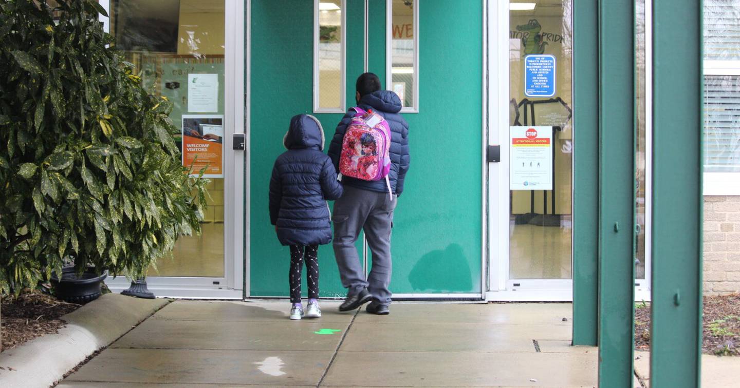 An adult walks a child to the front of a school building.