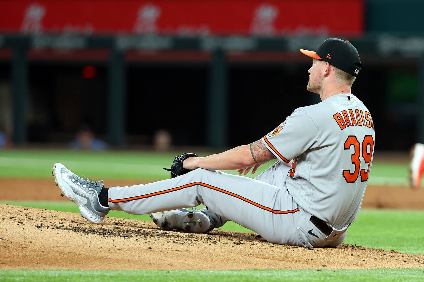 ARLINGTON, TEXAS - APRIL 03: Kyle Bradish #39 of the Baltimore Orioles sits on the mound after being hit by a line drive from Jonah Heim of the Texas Rangers in the second inning at Globe Life Field on April 03, 2023 in Arlington, Texas.