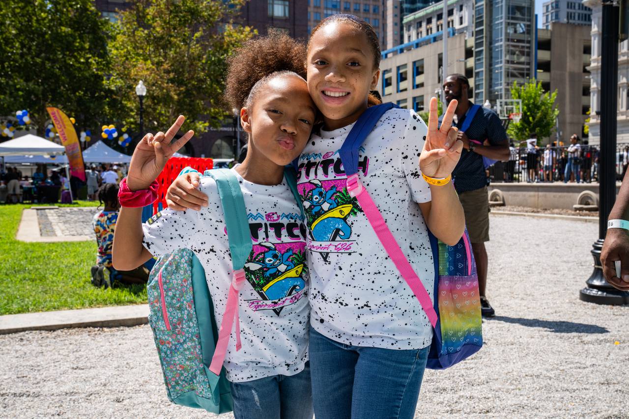 Nyel, 9, and Skyla, 10, smile and hold up peace signs for a photo with the new backpacks they received.