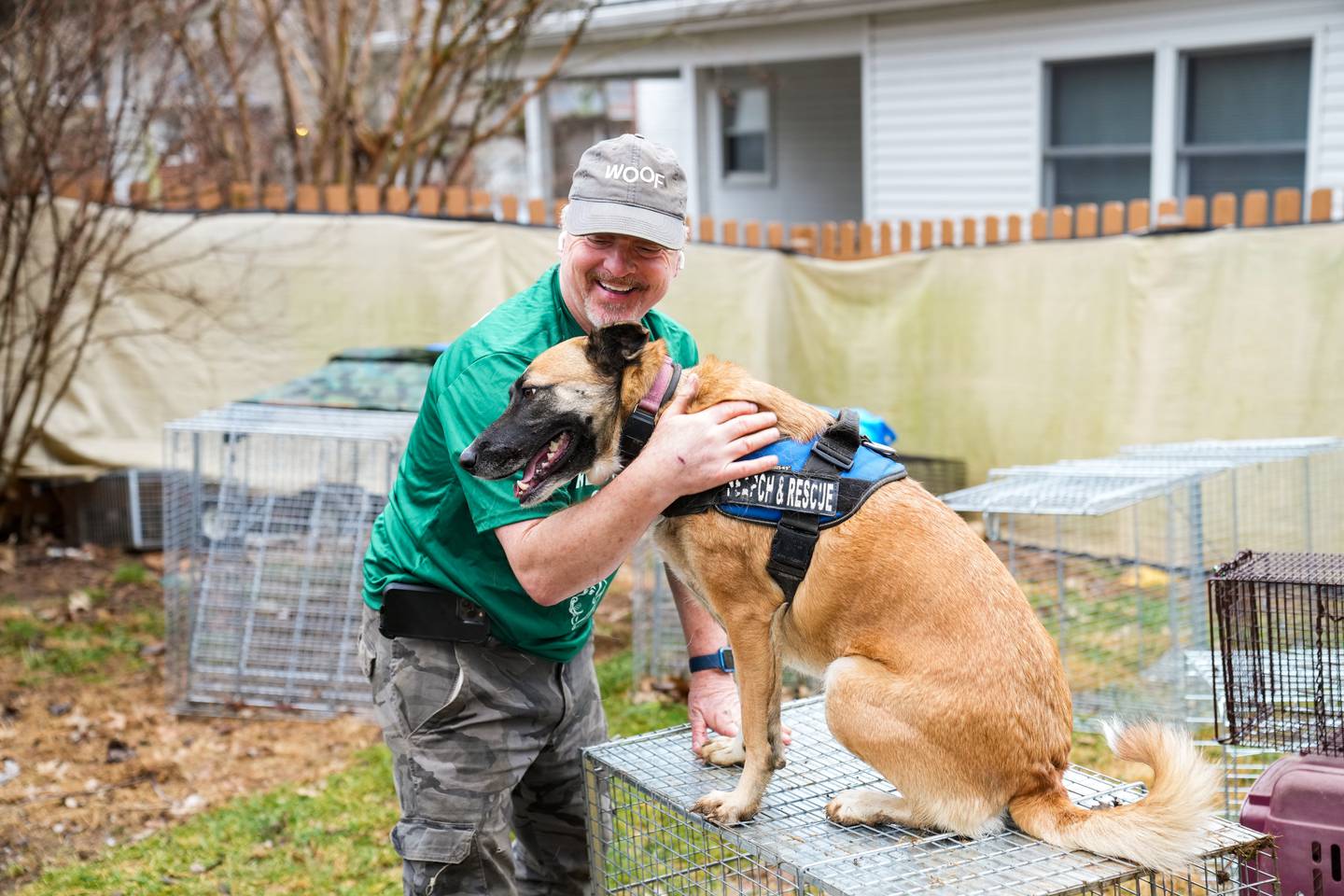 Man holds his search and rescue dog as it sits on top of a cage.