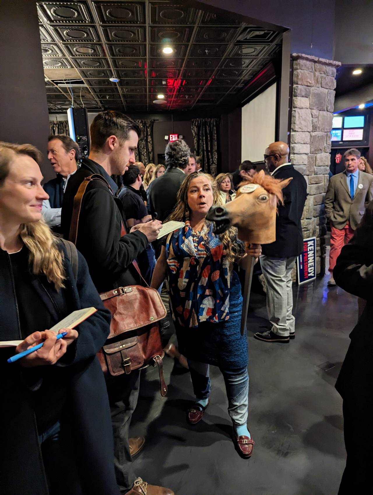 A woman totting a rubber horse's head on a stick talks to a reporter Monday night at the launch of Robert F. Kennedy Jr.'s campaign to get on the ballot as a candidate for president in 2024.