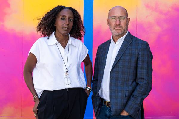 Tonya Miller Hall, left, and Todd Yuhanick pose for a portrait in front of a pink, orange and yellow watercolor-like mural.