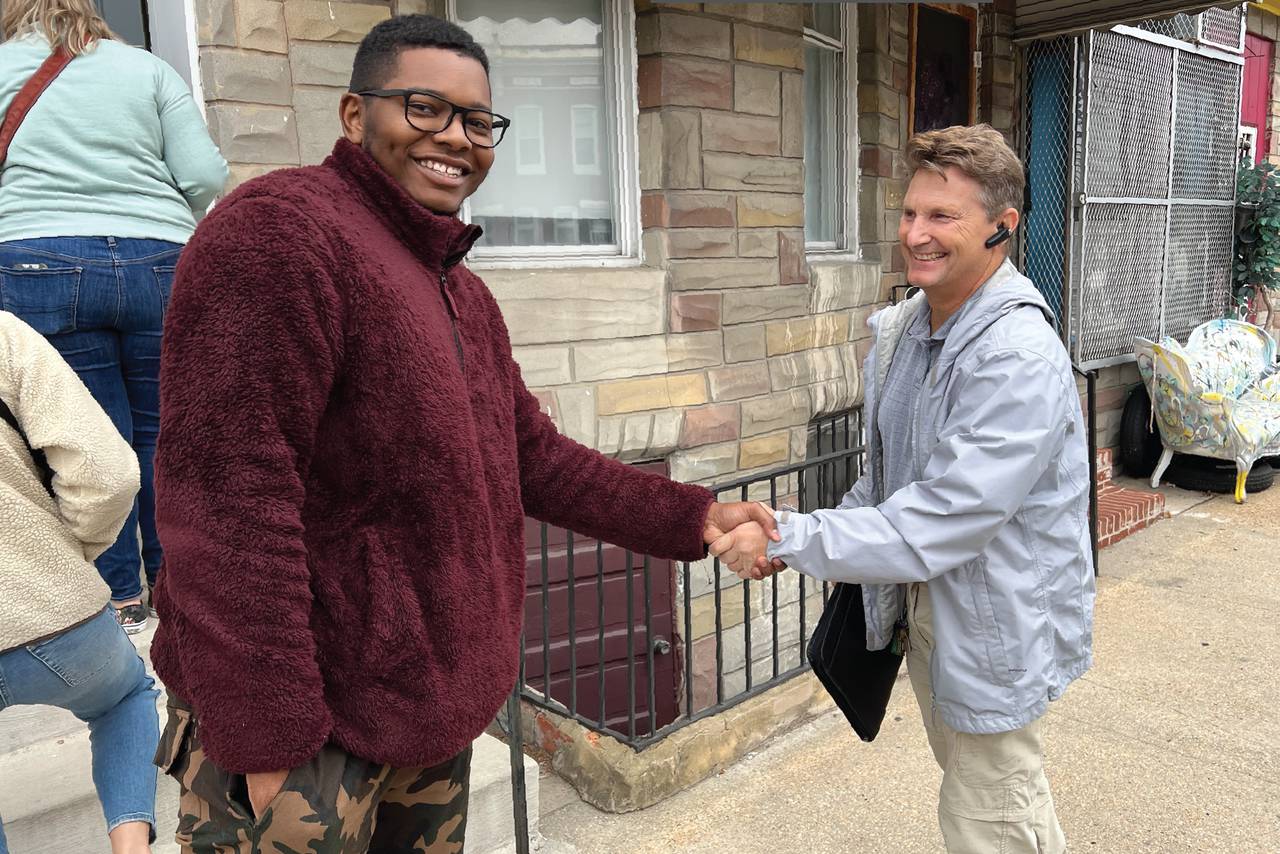 A local homebury and a representative from Habitat for Humanity Chesapeake shake hands in front of a newly purchased rowhome.