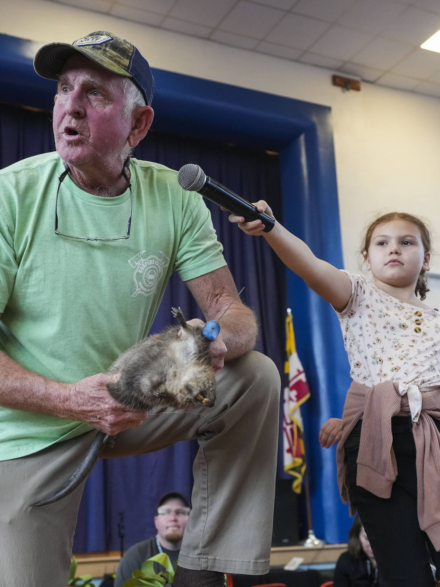 Kinsley Aaron, 10, holds the microphone for Buddy Flowers, 66, as he skins a muskrat for an audience explaining the process as he goes.