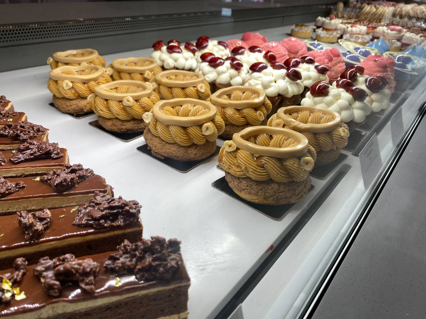 Pastries for sale appear behind glass, including chocolate eclairs, a brown butter-cream frosted pastry and a fluffy white frosted pastry with a red cherry on top.