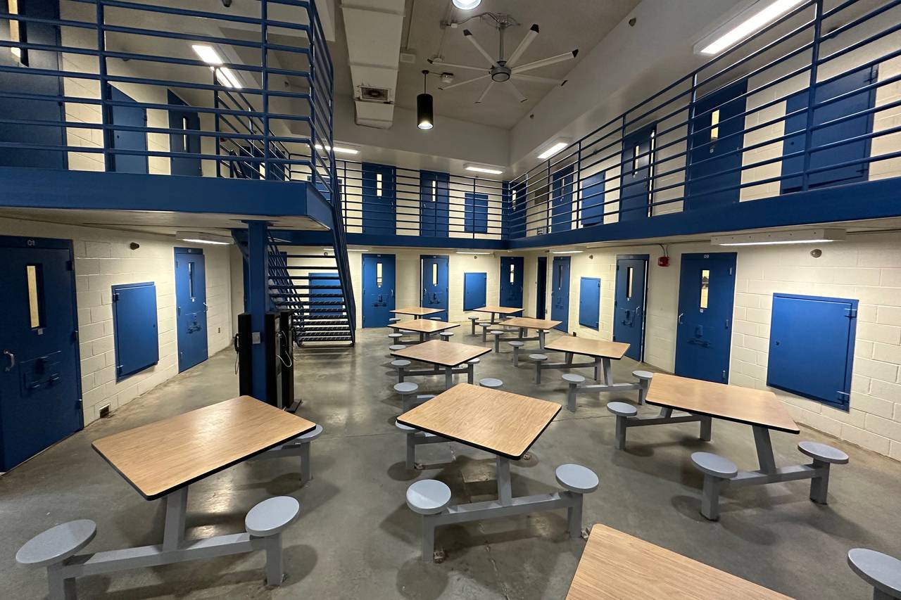 Photo of common area with tables and stools inside prison. Blue doors lead to cells off the ground floor and off a second floor walkway above.