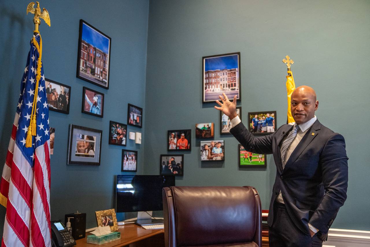 Gov. Wes Moore gestures to two photos that belonged to Pava LaPere and now hang in his office in the State House in Annapolis, Md., on Wednesday, Jan. 10, 2024. LaPere’s family gave the photos, which picture rowhomes in Baltimore, to Moore after her death in September 2023.