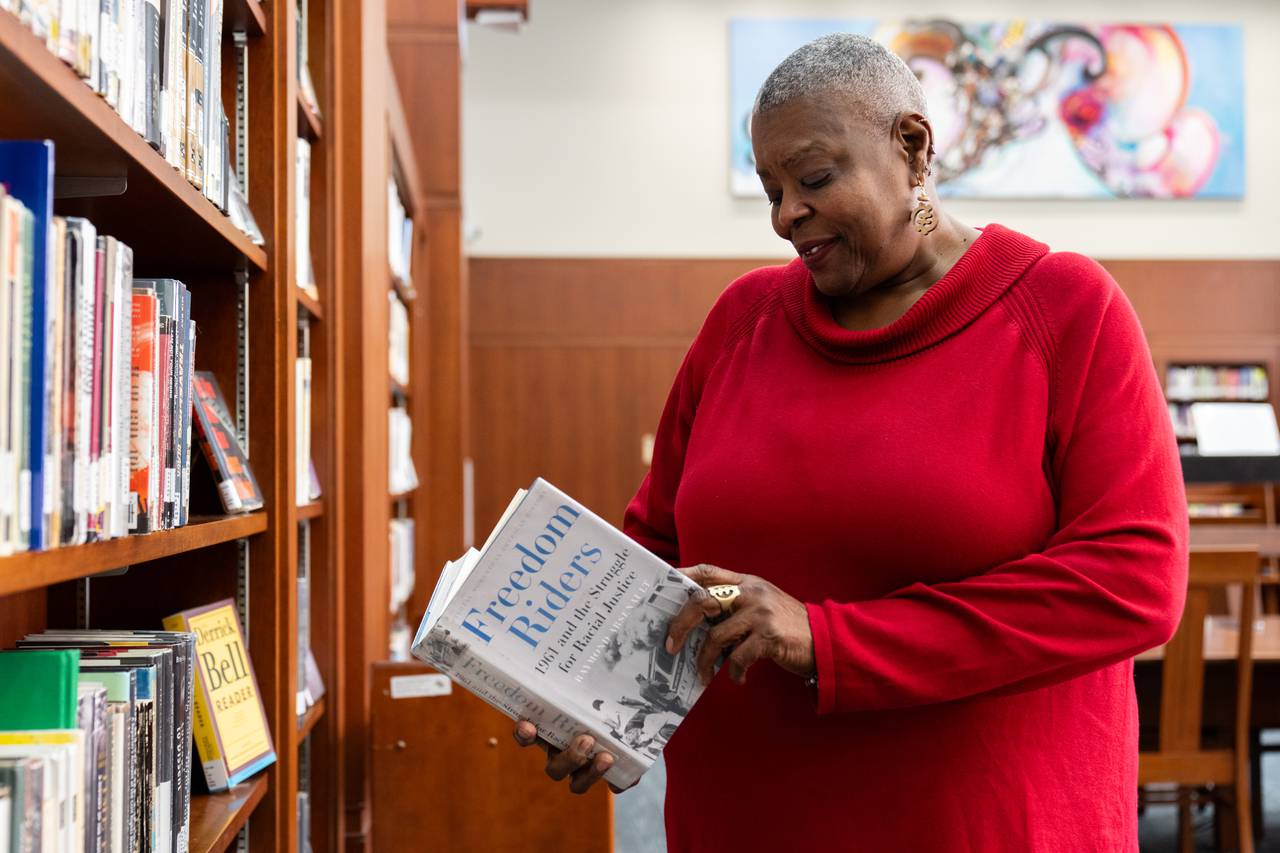 Vivian Fisher, in a red sweater, looks through “Freedom Riders” by Raymond Arsenault in the Enoch Pratt Central Library’s Juanita C. Burns Memorial African American Reading Room.