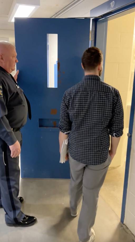 Photograph of white man in uniform on left holding open cell door for another white man in a collared shirt and slacks.