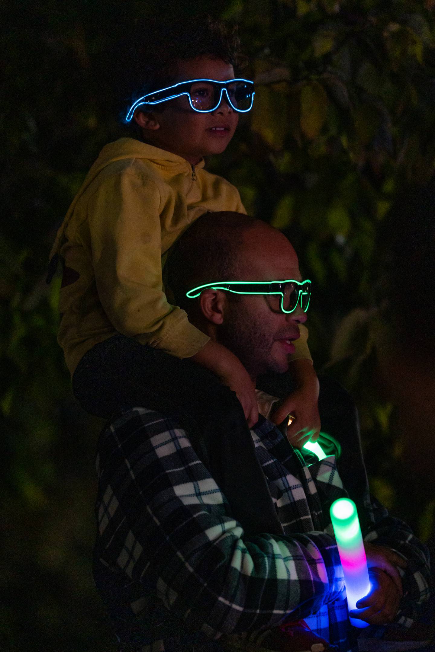 Jonathan Lynch and his son, Atlas Tao-Lynch, watch the Great Halloween Lantern Parade through neon glasses at Patterson Park on Saturday, Oct. 21, 2023.