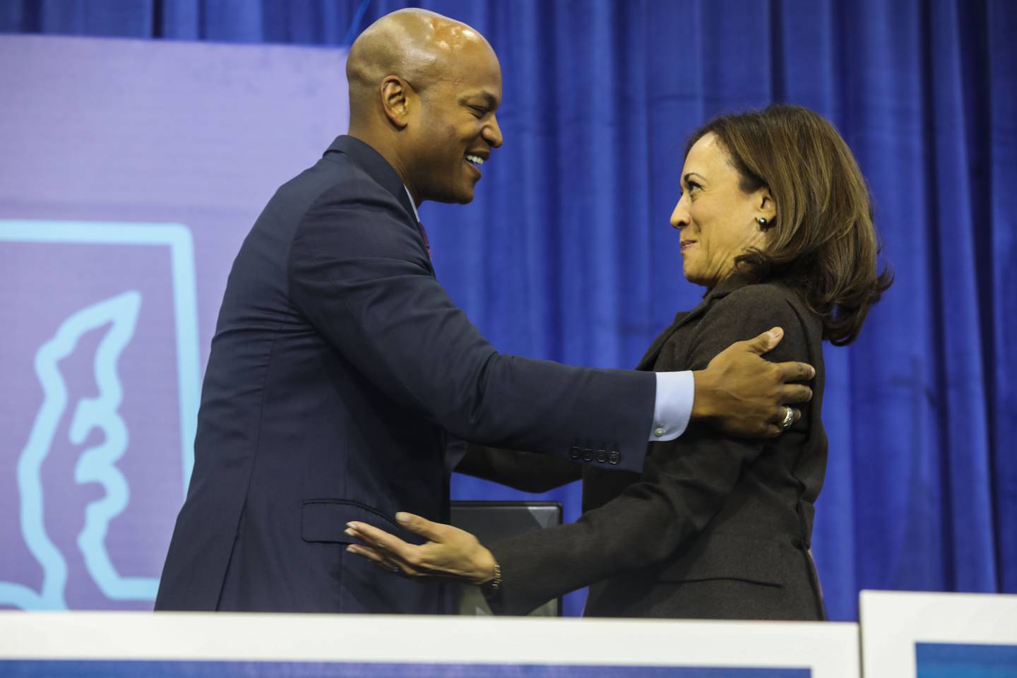 Kamala Harris and Wes Moore embrace in front of a blue background.