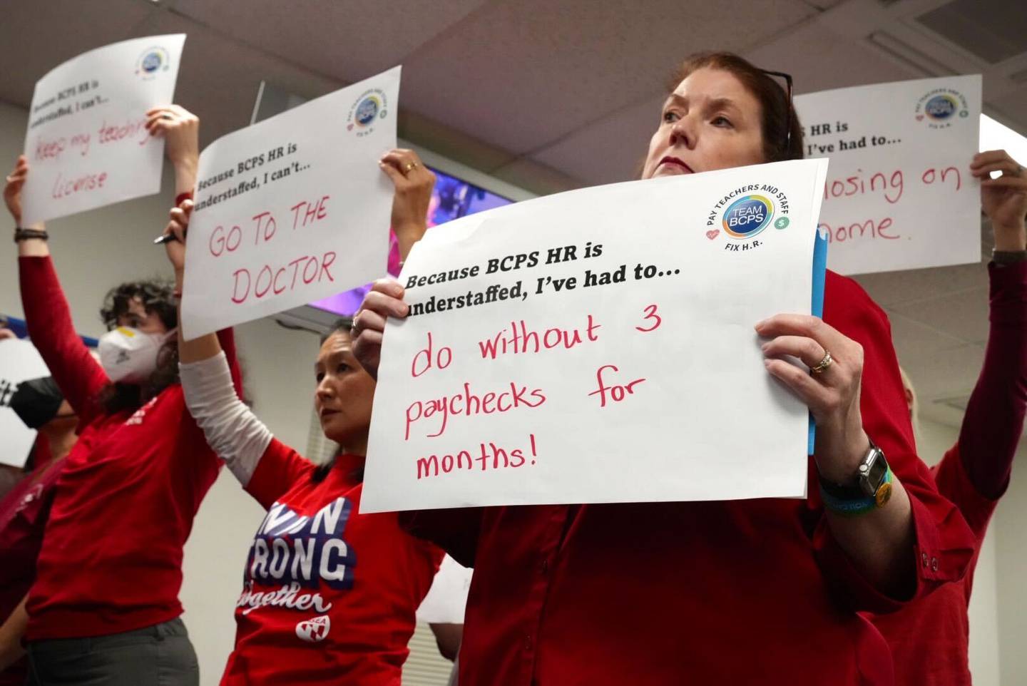 Kathleen Cave, right, and other Baltimore County Public School teachers stand together with signs calling out BCPS for pay being withheld, mistakes with benefits, delays in tuition reimbursement and stalled certification, during a school board meeting Tuesday, December 6.