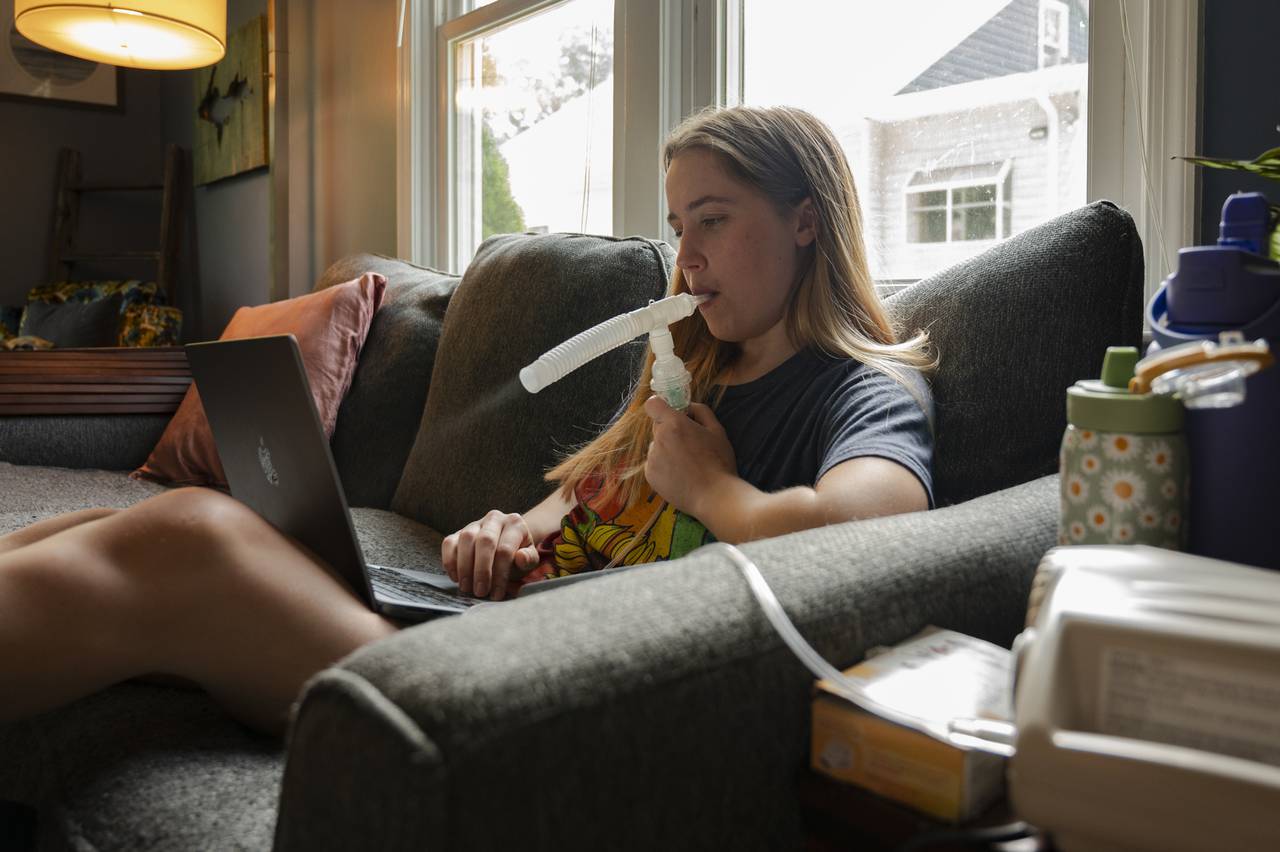 Anneliese Williams, 22, does a breathing treatment while she does work on a laptop. Her treatments have become her new normal as she lives her life around them.