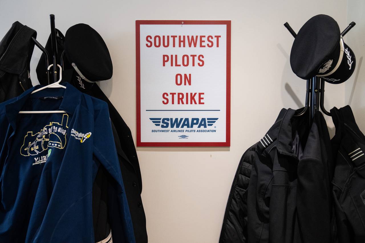 Pilots’ jackets and hats hang from a coat rack, framing a sign that says "Southwest pilots on strike."